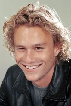 a close up of a person wearing a black jacket and smiling at the camera with long blonde hair