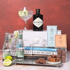 an assortment of liquors and books on a tray with wine glasses, lemon wedges, and gin