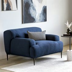 a blue chair sitting in front of a painting on the wall next to a table