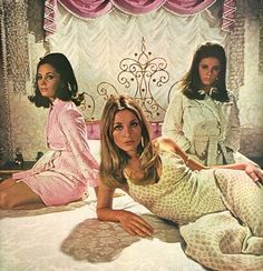 three women sitting on a bed in front of a window with pink curtains and drapes