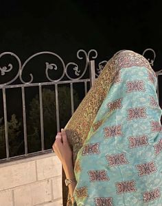 a woman wearing a shawl standing next to a brick wall and fence at night