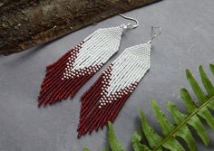 the red and white beaded earrings are hanging from a branch with leaves around it