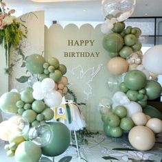 balloons are arranged in the shape of an arch for a happy birthday party with flowers and greenery