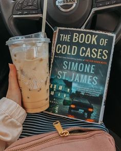 the book of cold cases sits next to a starbucks drink and a bag on a car seat