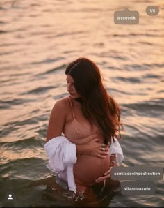 a pregnant woman standing in the water at sunset