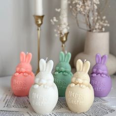 four small plastic easter eggs sitting on top of a table next to a white candle