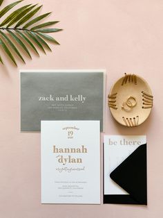 the wedding stationery is laid out on a pink background with a gold plate and palm leaf