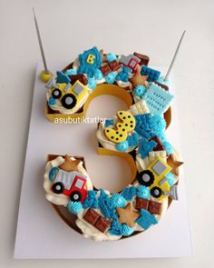 a cake shaped like the number three with cars and trucks on it, sitting on top of a white card