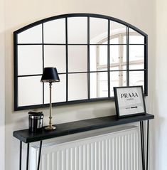 a mirror sitting above a radiator next to a table with a lamp on it