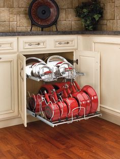 an open cabinet with red pots and pans in the bottom rack, on a wooden floor