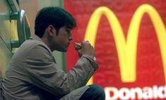 a man sitting on the ground eating food in front of a mcdonalds sign and holding a hot dog