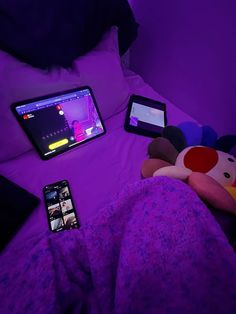 there are two cell phones and a laptop on the bed with stuffed animals next to it