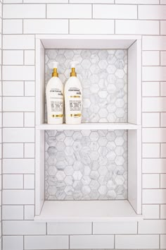 two bottles of shampoo and lotion sitting on shelves in a white tiled bathroom