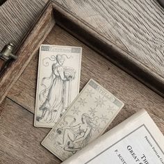 two tarot cards sitting on top of a wooden table next to an open book