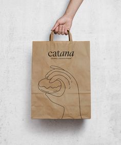 a person's hand holding a brown paper bag with the words catana on it