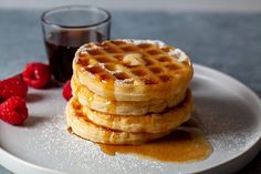 a stack of waffles sitting on top of a white plate next to raspberries