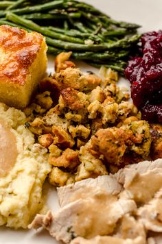 a white plate topped with meat, stuffing and veggies next to green beans