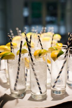 several glasses with lemons and black straws on a white tablecloth covered tray