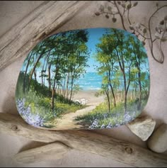 a painted rock sitting on top of a wooden branch next to some rocks and flowers