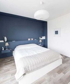 a white bed sitting in a bedroom next to a blue accent wall and wooden floors