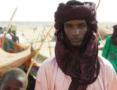 a man wearing a purple head scarf standing in front of other people on the beach