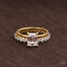 an engagement ring with a green emerald surrounded by white diamonds on a brown cloth background