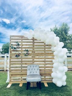 a chair sitting under an arch made out of wooden pallets with balloons attached to it