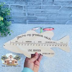 a person holding a wooden fish ruler with the words you're my greatest catch on it