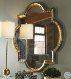 a mirror on the wall above a table with two lamps and a potted plant