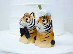 two small tiger figurines sitting next to each other on top of a cake