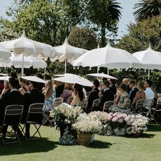 a group of people sitting under white umbrellas in the grass at an outdoor event