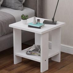 a white end table with magazines and a lamp on it in front of a couch