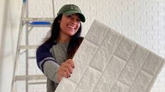 a woman is smiling while holding up a large piece of white tile in front of her