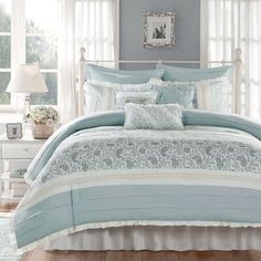 a bed with blue and white comforters in a bedroom next to a window on a wooden floor