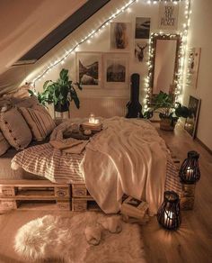 a bed with pillows and blankets in a room decorated with string lights, plants and pictures on the wall