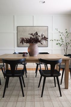 a dining room table with four chairs and a vase on the wall in front of it