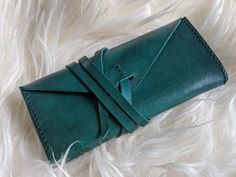 "Handmade genuine leather clutch with a wrap-style closure. This leather is vegetable tanned, hand dip-dyed for a one-of-a-kind color.  The stitching is also done by hand with a saddle-stitch method which is very resilient and will not unravel if one thread breaks. Edges are sanded and polished for a smooth look and feel. Perfect for stashing essential items for a night on the town or a minimalist who wants to keep things simple for daily carry. The gusseted sides in combination with the wrap-style closure allow for expansion when fitting larger items.  -  Emerald Green/Teal  - Dimensions: 7.25\"L x 3\"H x 1.25\"W - Gusseted sides will extend to 2.25\" when opened fully  - Strap is approximately 27\" and can be cut shorter as desired  - Can fit most standard-sized smart phones *As with dye Green Leather Clutch With Card Slots, Daily Carry, Saddle Stitch, Leather Clutch Purse, Leather Clutch Bag, Dip Dyed, Smart Phones, Envelope Clutch, Essential Items