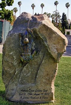 a large rock in the grass with a statue on it's side and palm trees behind it