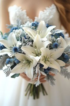 a bridal bouquet with white lilies, blue berries and greenery is held by a bride