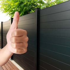 a hand giving the thumbs up sign in front of a black fence with green plants