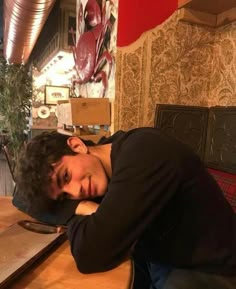 a man laying his head on top of a wooden table next to a potted plant