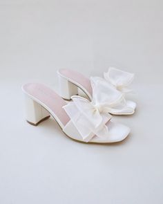 a pair of white shoes with a large bow on the back and heel, all in satin material