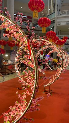 red and pink flowers are on display in a building with chinese lanterns hanging from the ceiling