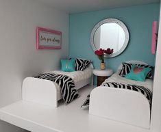 two beds with zebra print covers and pillows in a small room next to a mirror