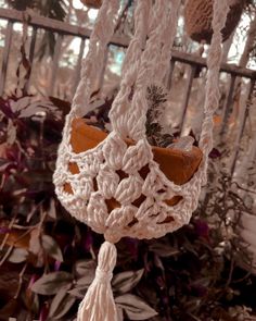 a white crocheted hanging planter in front of some plants