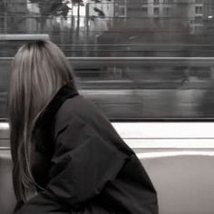 a woman sitting on a bench in front of a train window looking out the window