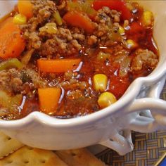 a white bowl filled with meat and veggies next to crackers on a plate