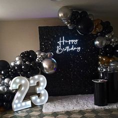 a birthday party with balloons and lights on the wall, black and silver decorations in front of it