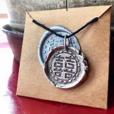 a silver pendant with chinese writing on it sitting on a brown paper box next to a potted plant