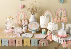 a table topped with lots of cake and cupcakes next to a rainbow banner